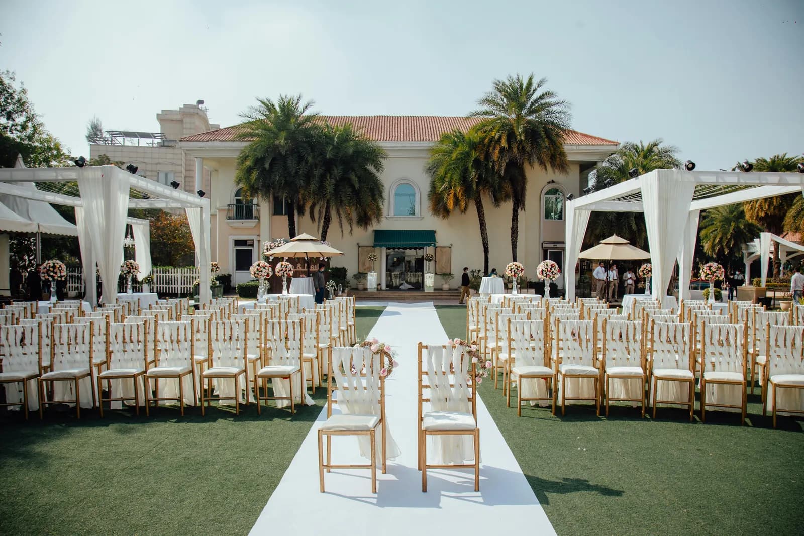 Rows of white chairs and an aisle on a lawn in front of a colonial-style hotel