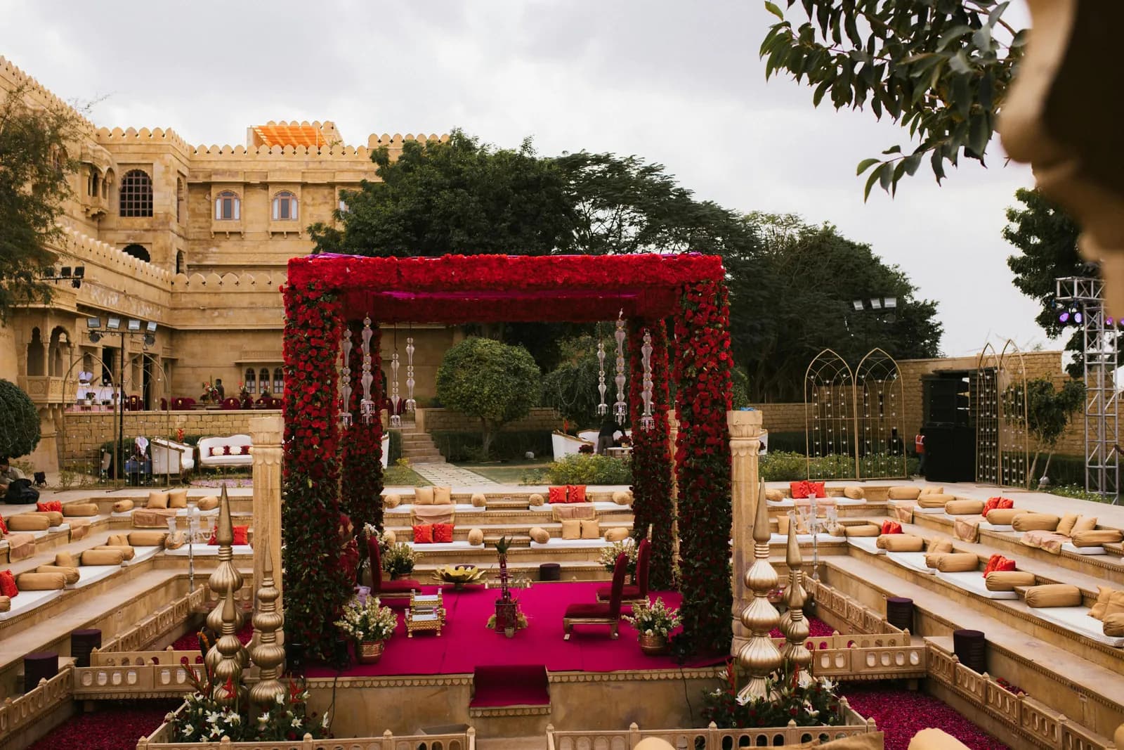 Red floral mandap with floor seating in a sandstone palace courtyard