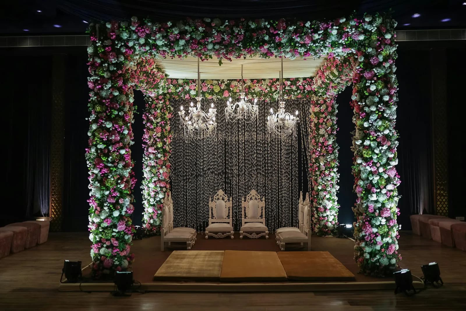 Indoor mandap framed in pink and white flowers with crystal chandeliers