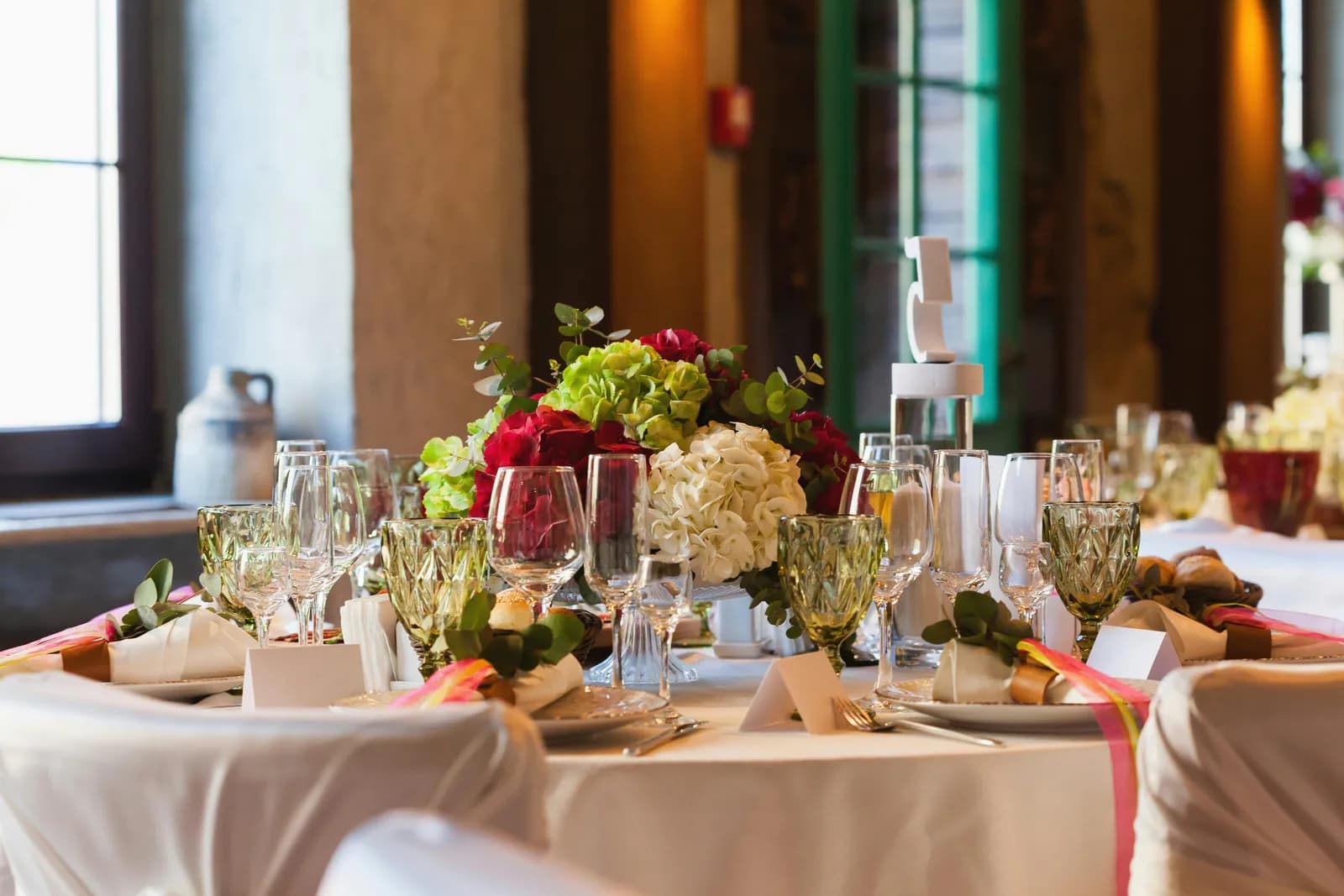 Dining table laid with glassware and a floral centrepiece beside a window