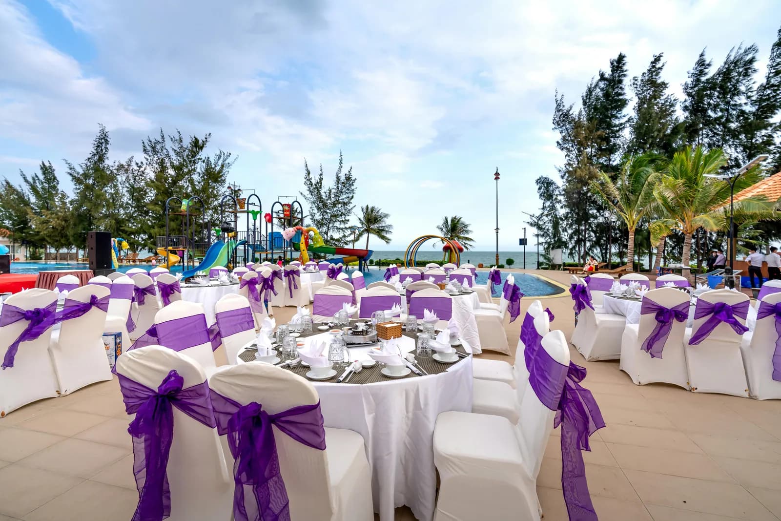 Round tables with purple sashes on a poolside lawn by the sea