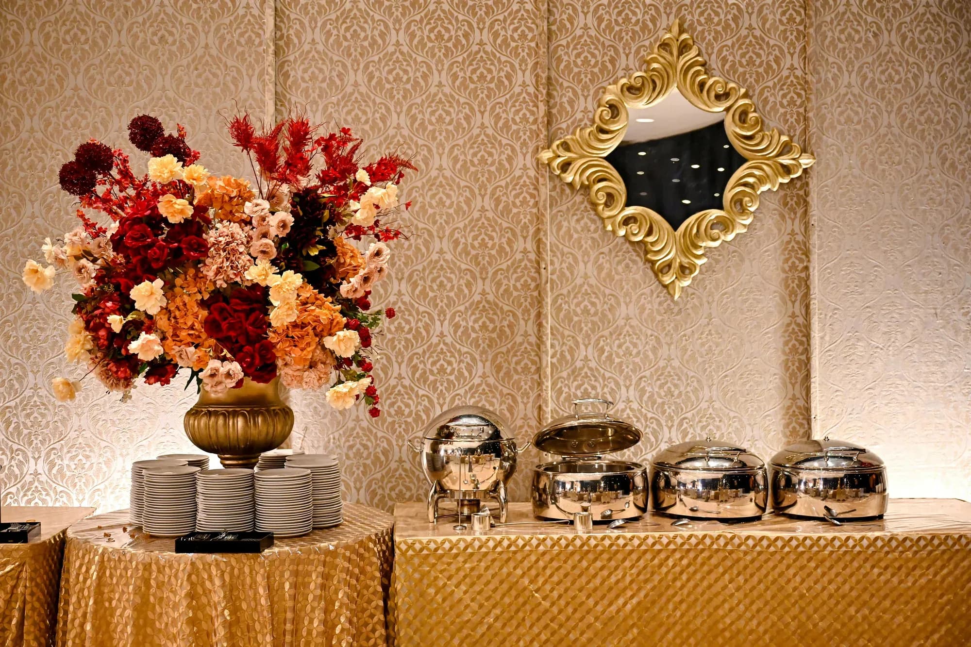 Silver chafing dishes beneath a floral arrangement and a gilded mirror