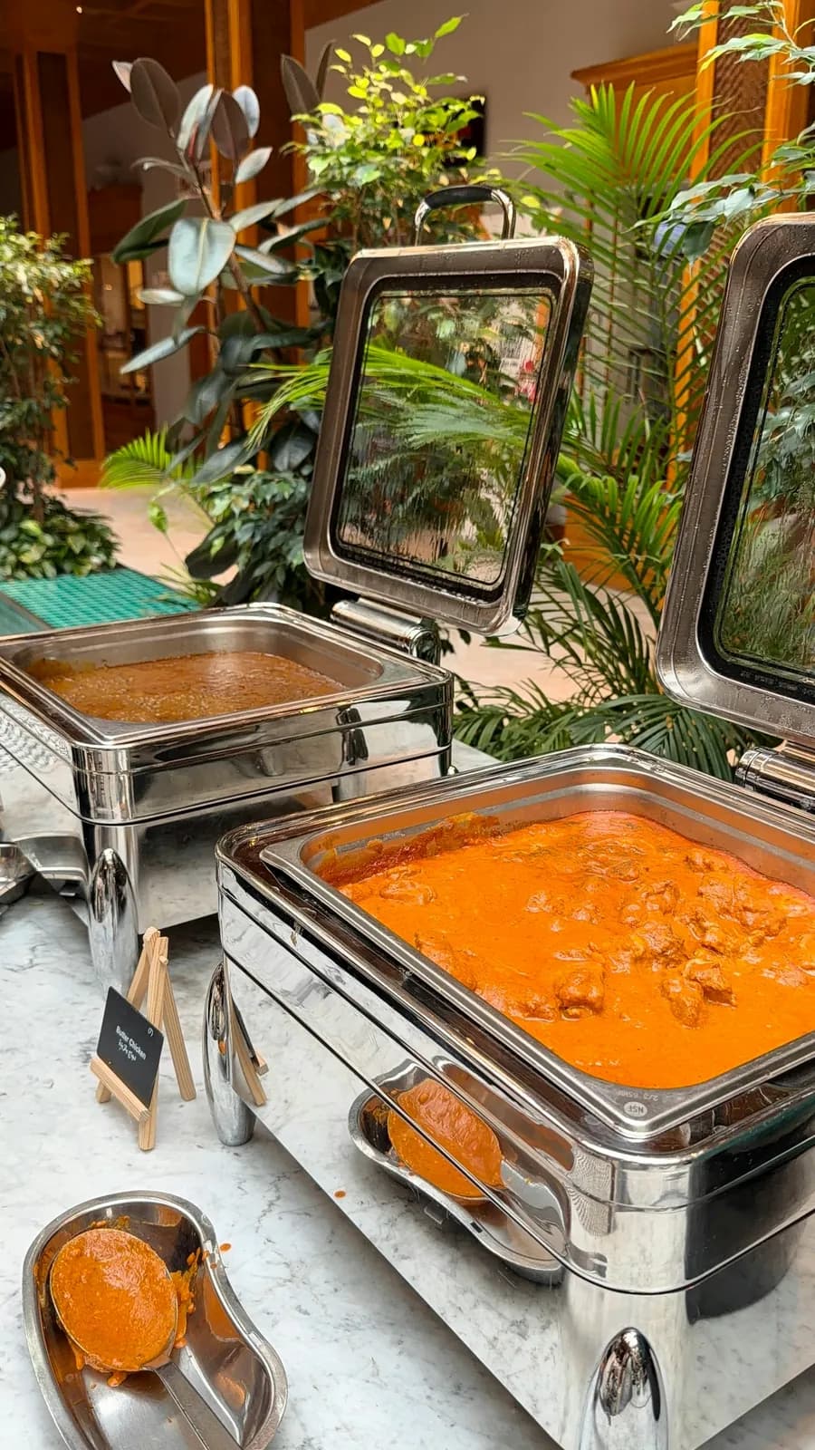 Chafing dishes of curry on a buffet counter set among potted greenery