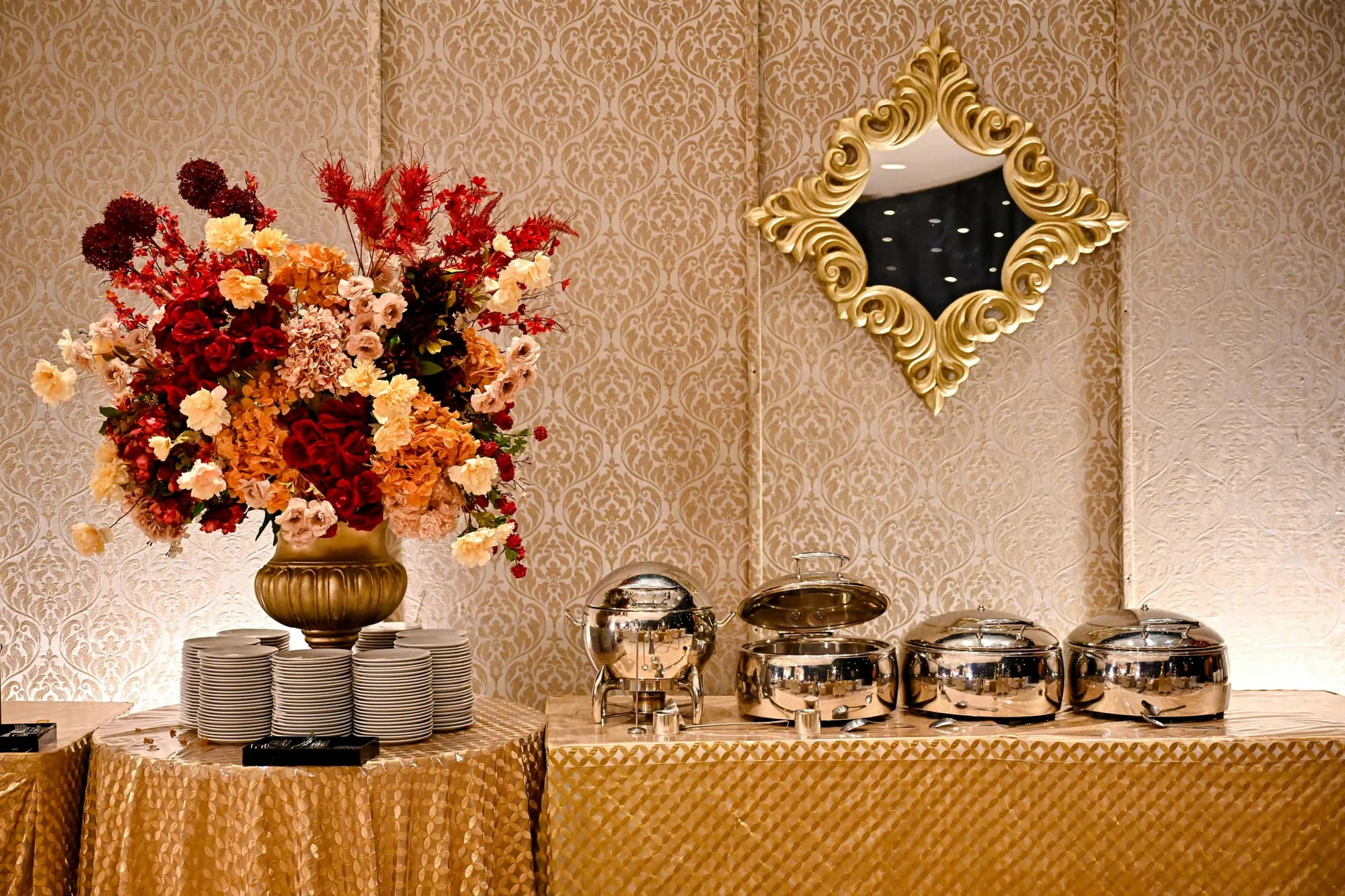 Silver chafing dishes beneath a floral arrangement and a gilded mirror