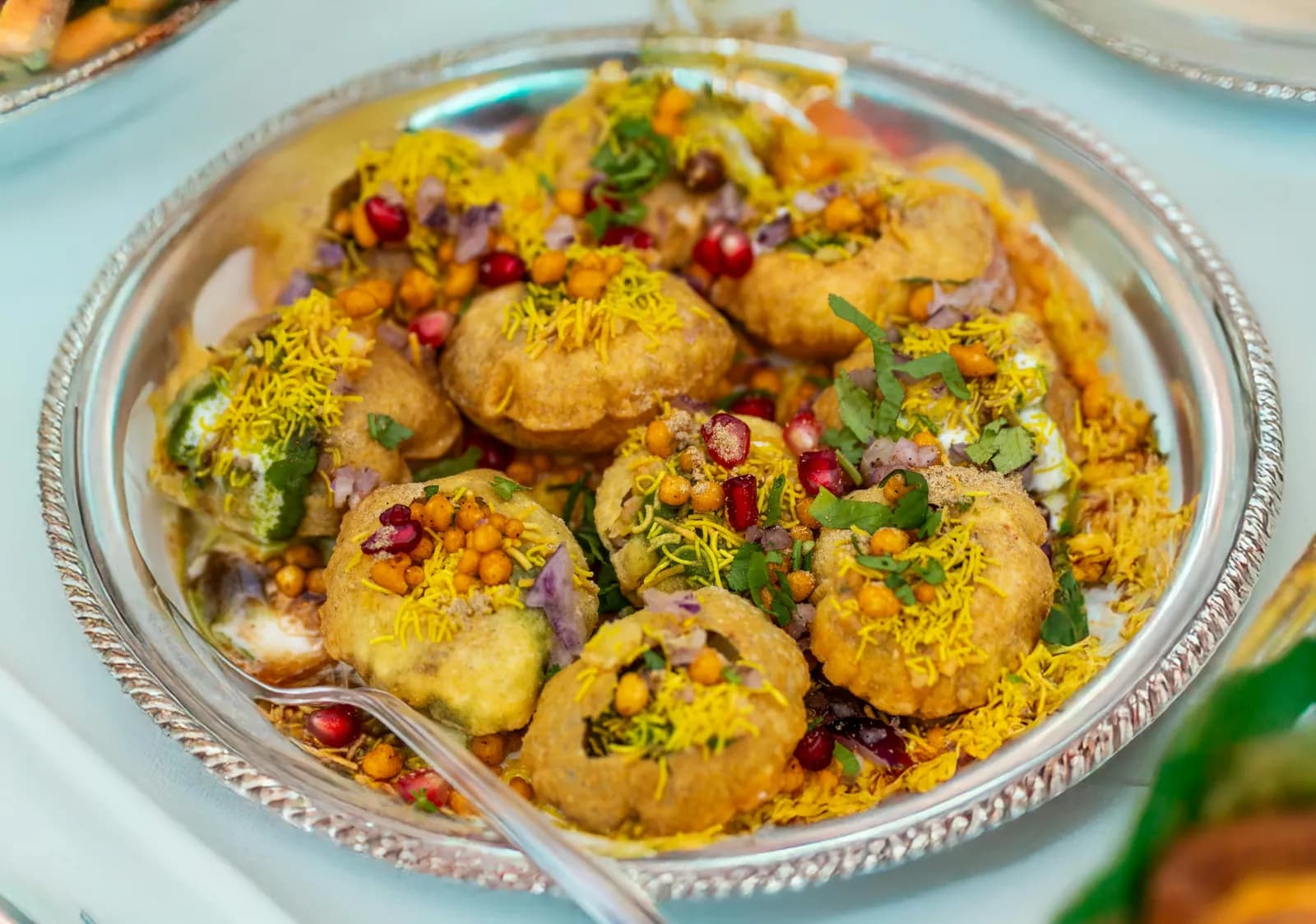 Silver platter of chaat topped with sev, pomegranate and coriander