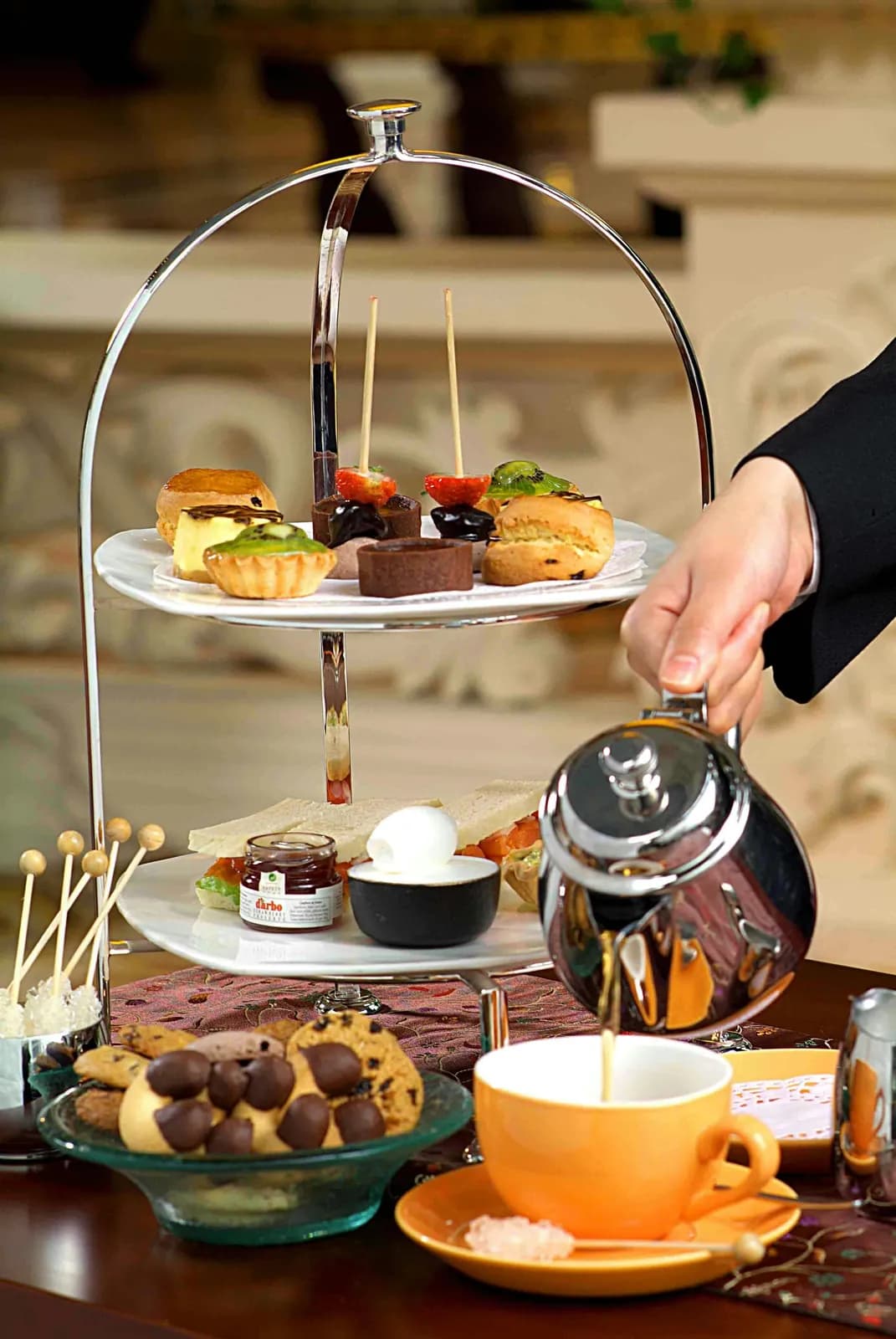 Tiered hi-tea stand of sandwiches and pastries as tea is poured