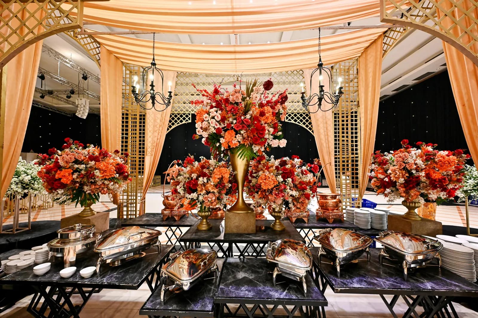 Reception hall with floral centrepieces and buffet chafing dishes under draped canopies