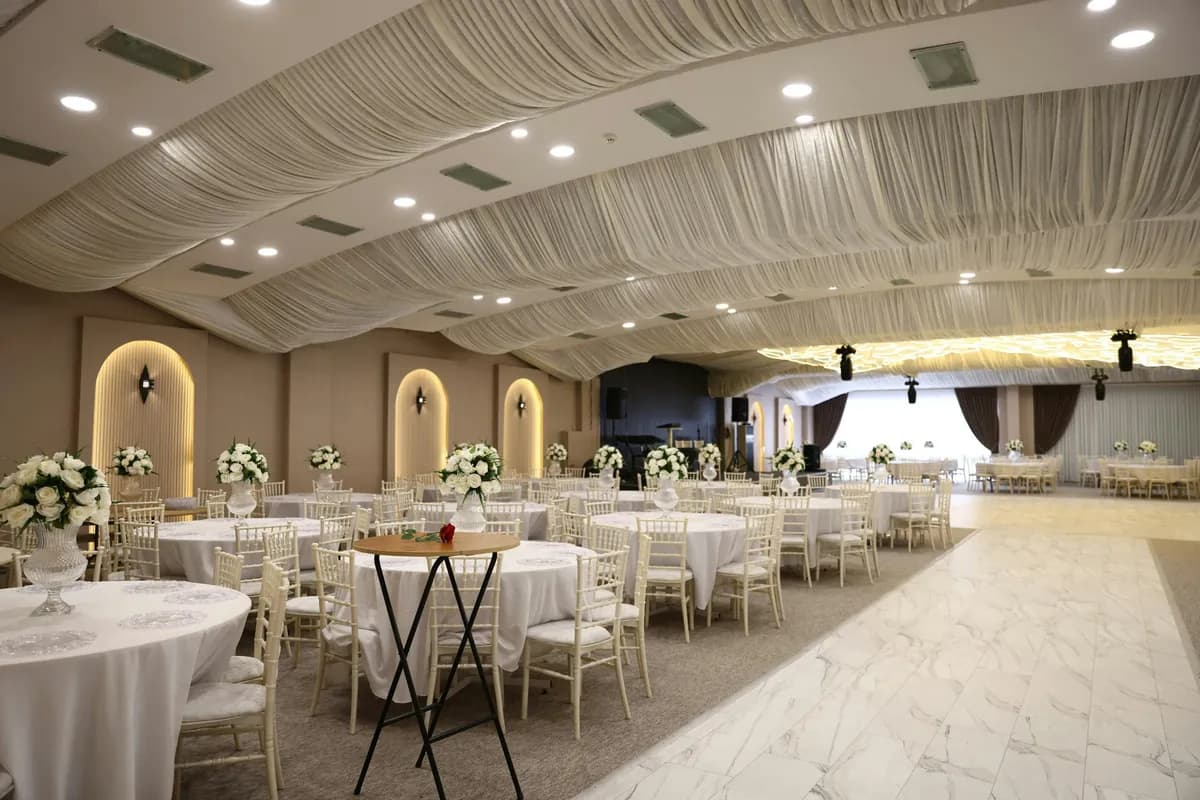 Banquet hall with round tables, white chairs and a draped ceiling