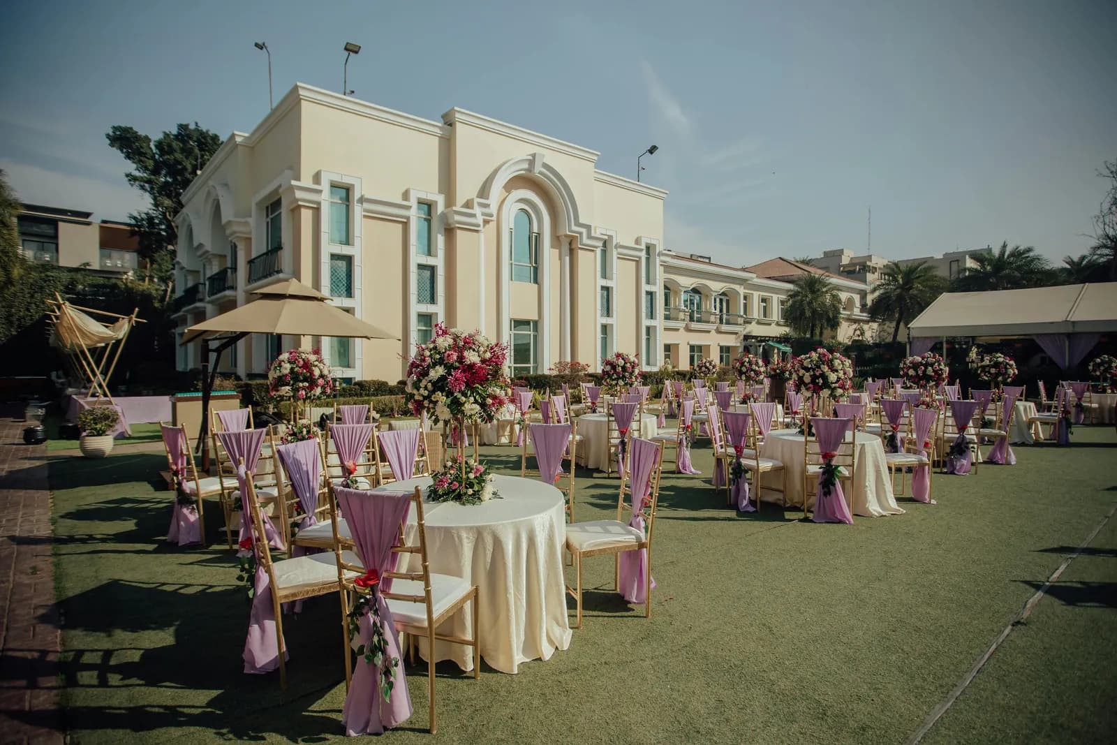 Round tables with floral centrepieces on a lawn beside a hotel facade